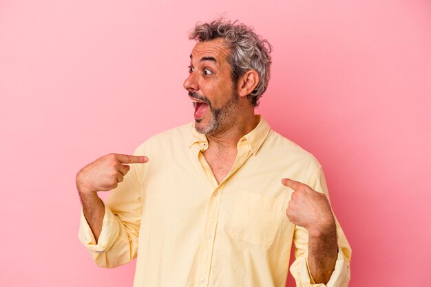 Kaukasischer Mann mittleren Alters isoliert auf rosafarbenem Hintergrund überrascht, wie er mit dem Finger zeigt und breit lächelt.