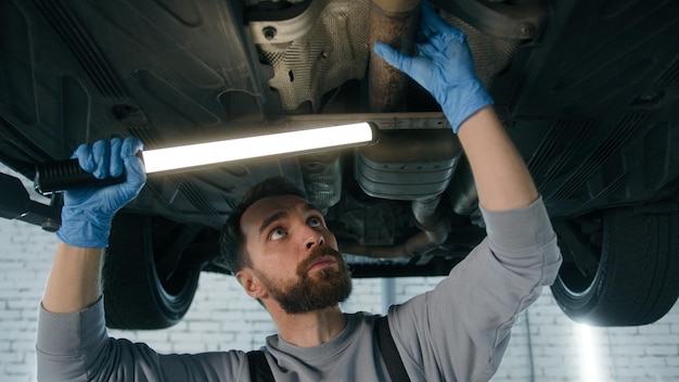 Kaukasischer Mann, Reparaturmann, Automechaniker, der unter einem Fahrzeug in der Garage arbeitet.