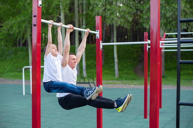 Kaukasischer Mann trainiert einen Jungen auf der horizontalen Stange auf dem Spielplatz Vater und Sohn gehen zum Sport im Freien