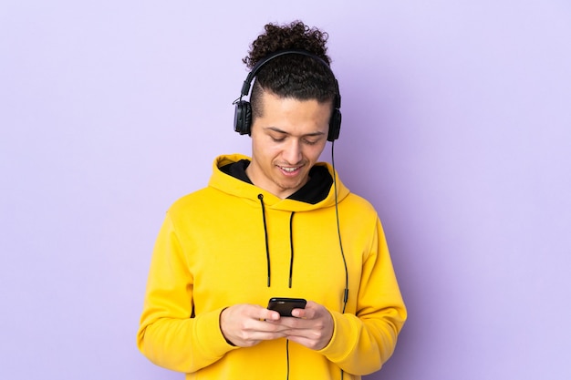 Kaukasischer Mann über isolierter lila Wand, die Musik hört und auf Handy schaut