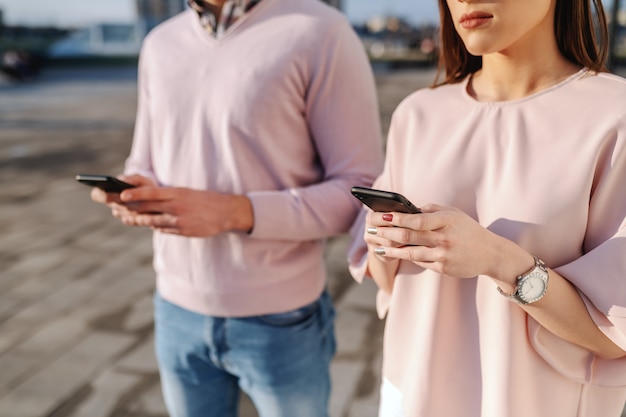 Kaukasischer Mann und Frau, die Smartphones verwenden, während sie nebeneinander im Freien stehen