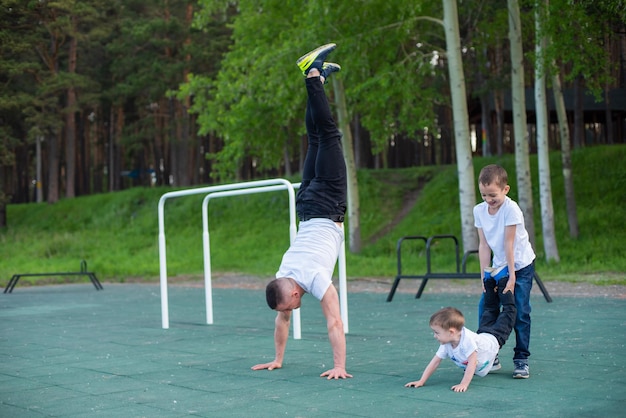 Kaukasischer Mann unterrichtet Söhne im Handstand auf dem Spielplatz im Freien