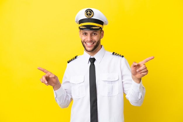 Kaukasischer Pilot des Flugzeugs lokalisiert auf gelbem Hintergrund, der mit dem Finger auf die seitlichen und glücklichen zeigt