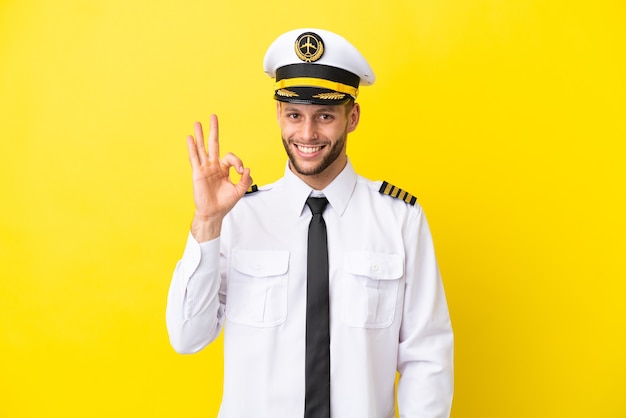 Kaukasischer Pilot des Flugzeugs lokalisiert auf gelbem Hintergrund, der okayzeichen mit den Fingern zeigt