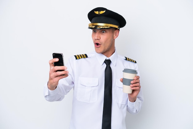 Kaukasischer Pilot des Flugzeugs lokalisiert auf weißem Hintergrund, der Kaffee zum Mitnehmen und ein Handy hält