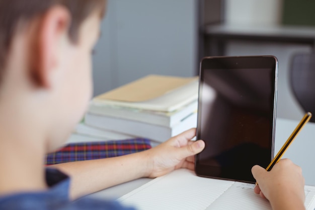 Kaukasischer Schüler sitzt im Klassenzimmer am Schreibtisch und benutzt ein Tablet, mit Platz für Kopien auf dem Bildschirm