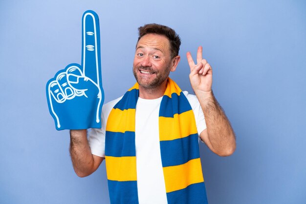 Kaukasischer Sportfan mittleren Alters isoliert auf blauem Hintergrund lächelnd und Victory-Zeichen zeigend