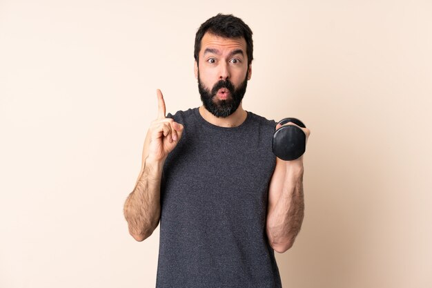 Kaukasischer Sportmann mit Bart, der Gewichtheben über Wand macht, um die Lösung zu verwirklichen, während er einen Finger anhebt