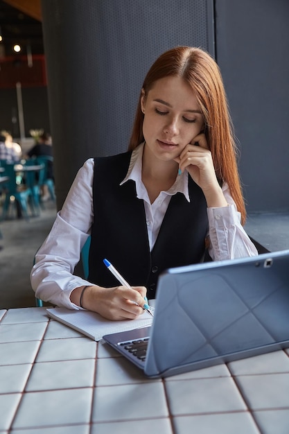 Kaukasischer Student, der am Tisch des Cafés sitzt und mit Laptop Hausaufgaben macht