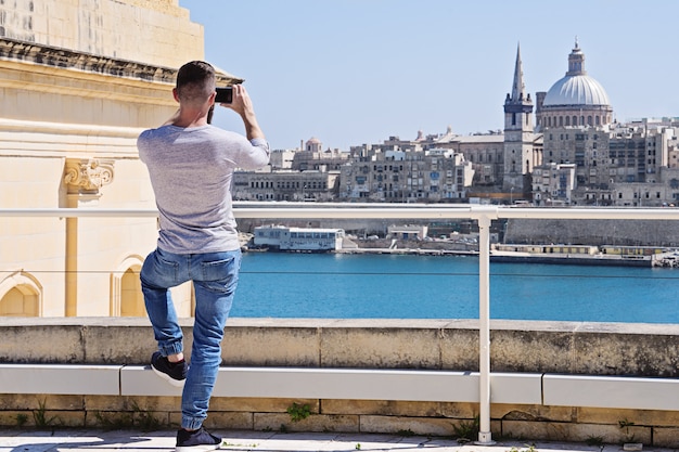 Kaukasischer Studentenmann hinten mit Smartphone machen Foto von Valletta-Skylinen