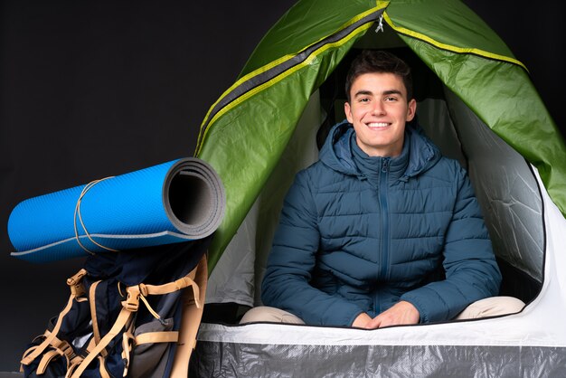 Foto kaukasischer teenager-mann in einem grünen zelt des campings auf schwarzer wand, die die arme in frontalposition verschränkt hält