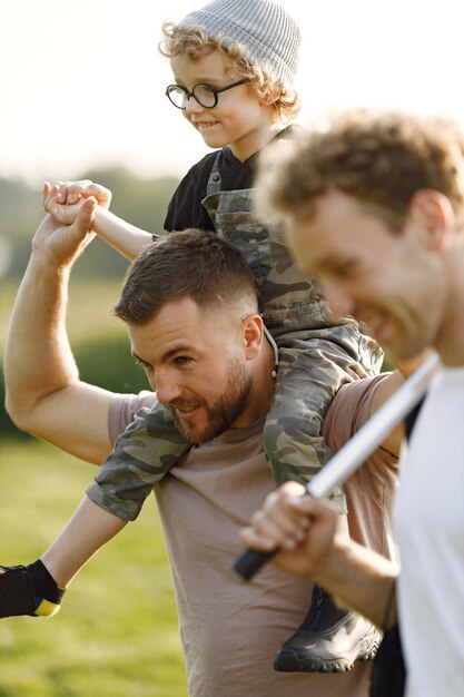 Kaukasischer Vater und Kinderjunge spielen und lachen zusammen Vater hält seinen Sohn auf den Schultern im Sommerpark im Freien Zwei Männer und ein kleiner Junge gehen spazieren