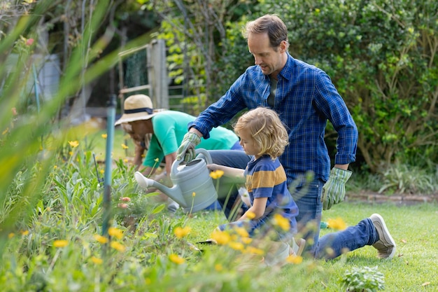 Foto kaukasischer vater und sohn im garten, bewässerung von pflanzen und gartenarbeit mit ihrer familie. glückliche familie mit drei generationen, die gemeinsam zeit zu hause verbringt.