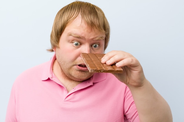 Kaukasischer verrückter blonder dicker Mann, der eine Schokoladentafel hält