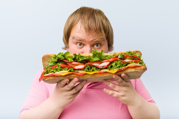 Kaukasischer verrückter blonder Mann, der ein riesiges Sandwich hält