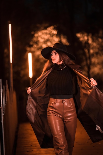 Kaukasisches brünettes Mädchen mit Hut, das nachts in einem Park geht. Winterabendmode