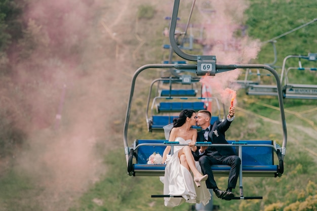 Kaukasisches Hochzeitspaar, das Seilbahn mit buntem Rauch in ihren Händen reitet.