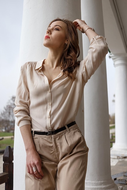 Kaukasisches hübsches Mädchen mit gewellten Haaren der roten Lippen in der stilvollen beige Bluse draußen