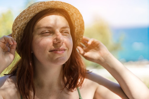 Kaukasisches junges schönes rothaariges Mädchen in einem Strohhut lächelnd, einen Urlaub am Meer genießt.