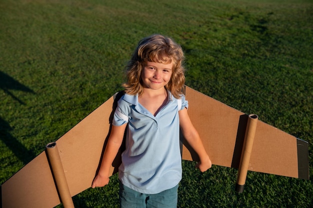 Kaukasisches Kind, das mit Spielzeugflugzeug auf Himmelshintergrund draußen auf einem grasbewachsenen Sommerhügel spielt und davon träumt