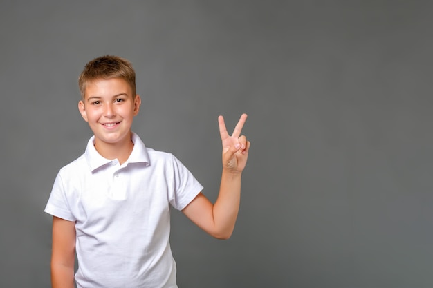 Kaukasisches Kind, das über lokalisiertem grauem Hintergrund steht und Siegeszeichen zeigt