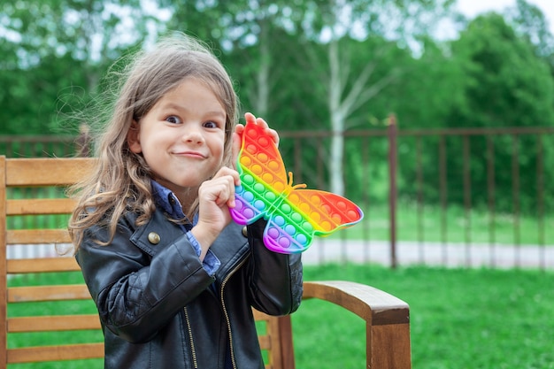 Kaukasisches kleines Mädchen spielt mit Pop-It-Silikon trendiges Regenbogen-Colow-Spielzeug