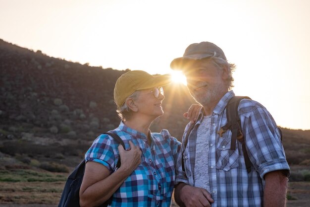 Kaukasisches lächelndes älteres Paar mit Rucksack, das bei Sonnenuntergang in der Landschaft unterwegs ist