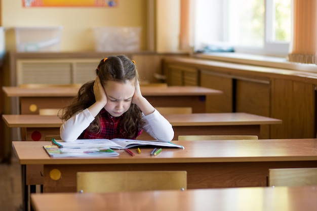 Kaukasisches Mädchen, das am Schreibtisch im Klassenzimmer sitzt und hart ist, Lektionen zu lernen. Prüfungsvorbereitung, Tests