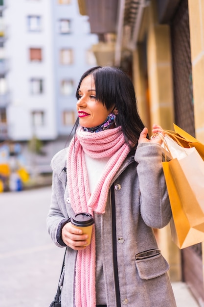 Kaukasisches Mädchen, das in der Stadt mit Papiertüten und einem Kaffee zum Mitnehmen einkauft