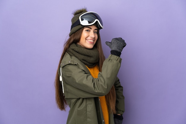 Kaukasisches Mädchen des Skifahrers mit Snowboardbrille lokalisiert auf lila Hintergrund stolz und selbstzufrieden