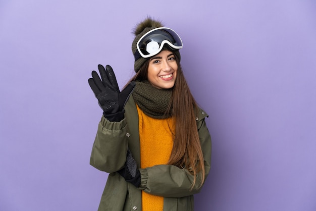 Kaukasisches Mädchen des Skifahrers mit Snowboardbrille lokalisiert auf lila Wand, die fünf mit den Fingern zählt