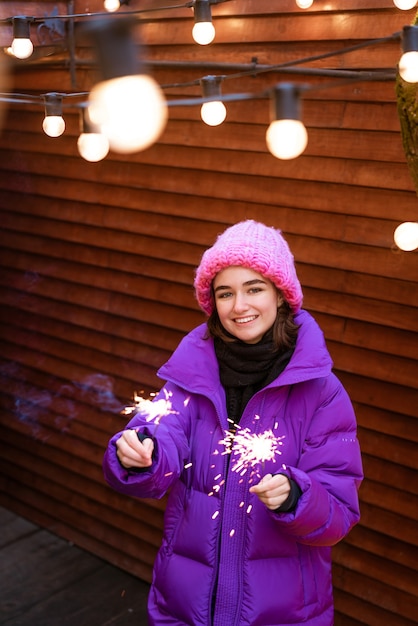 Kaukasisches Mädchen hat Spaß im Winter auf der Straße mit Wunderkerzen in der Hand und lächelt vor Glück w...