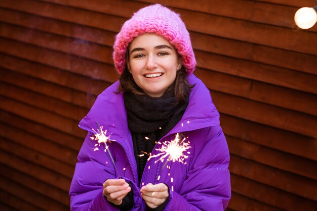 Kaukasisches Mädchen hat Spaß im Winter auf der Straße mit Wunderkerzen in der Hand und lächelt vor Glück w...