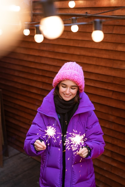 Kaukasisches Mädchen hat Spaß im Winter auf der Straße mit Wunderkerzen in der Hand und lächelt vor Glück w...