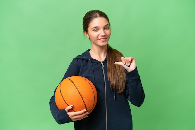 Kaukasisches Mädchen im Teenageralter, das Basketball vor isoliertem Hintergrund spielt, stolz und selbstzufrieden