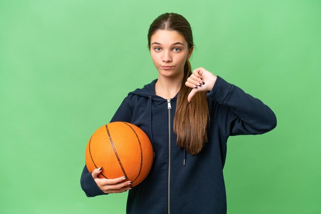 Kaukasisches Mädchen im Teenageralter, das Basketball vor isoliertem Hintergrund spielt und den Daumen nach unten mit negativem Ausdruck zeigt