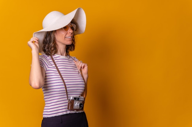 Kaukasisches Mädchen im Touristenkonzept mit Hut und Fotokamera auf gelbem Hintergrund