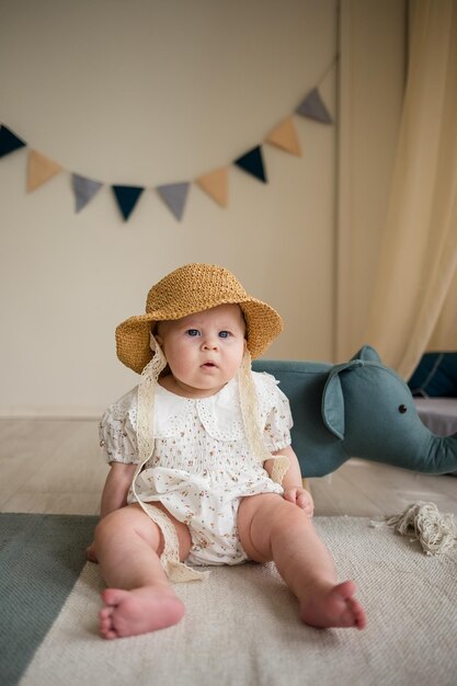 Foto kaukasisches mädchen in bodysuit und strohhut, das im kinderzimmer auf dem boden sitzt