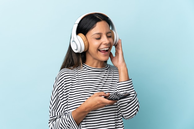 Kaukasisches Mädchen lokalisiert auf blauem Hintergrund, der Musik mit einem Handy und Gesang hört