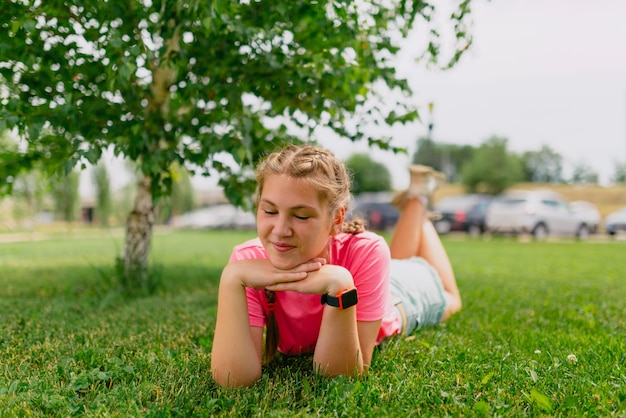 Kaukasisches Mädchen mit Sommersprossen und in einem rosa T-Shirt liegt auf dem Gras. Studentin lächelt und genießt das schöne Sommerwetter.