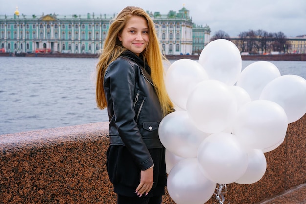 Kaukasisches Mädchen mit weißen Ballons, die am Nachmittag am Fluss am Ufer der Stadt in einem ...