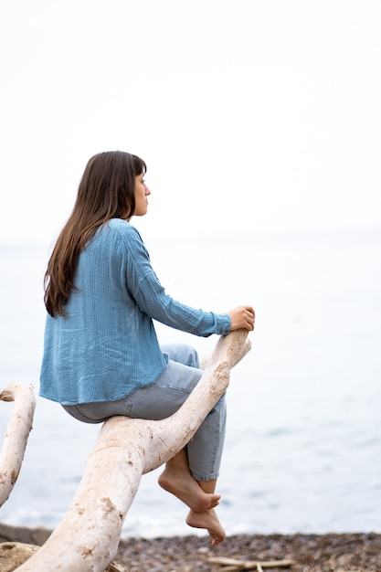 Foto kaukasisches mädchen sitzt auf einem baumstamm am strand mit blick auf das meer im frühjahr