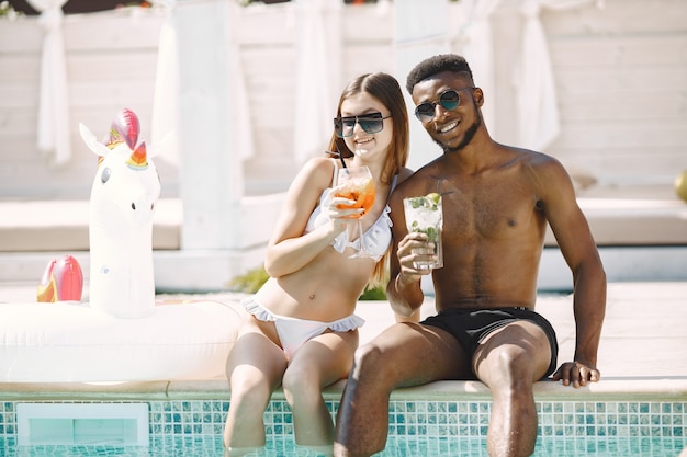 Kaukasisches Mädchen und ihr afroamerikanischer Freund, der sich in der Nähe des Swimmingpools entspannt. Mädchen mit weißer Badebekleidung und Sonnenbrille