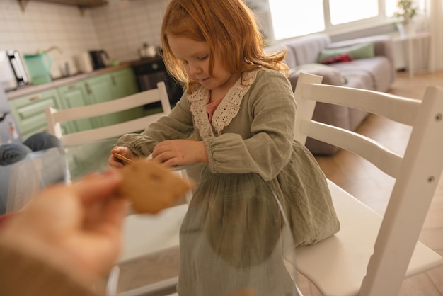 Kaukasisches rothaariges Kleinkind kaut Kekse mit Vergnügen und Vergnügen, während es am Tisch sitzt Snack-Konzept