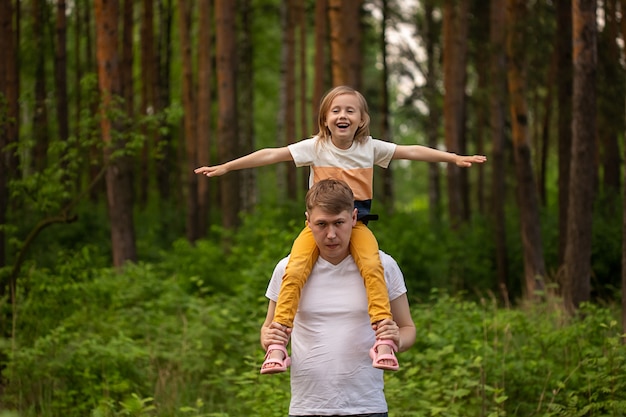 Kaukasisches süßes kleines Mädchen, das auf den Schultern ihres Vaters im Wald sitzt