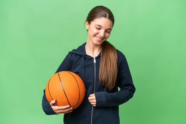 Kaukasisches Teenagermädchen, das Basketball über isoliertem Hintergrund spielt und viel lächelt