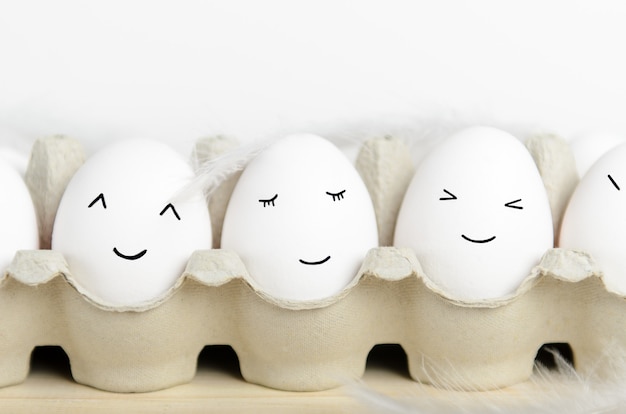 Kawaii Gesicht Eier in einem Karton mit Federn auf einem weißen Hintergrund schließen. Konzept Cartoons, Lebensmitteldekoration für Kinder