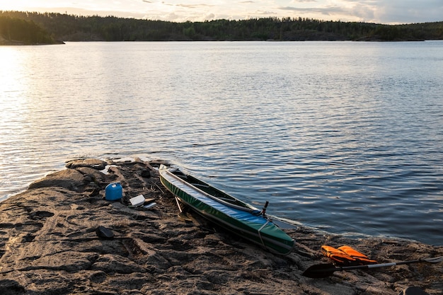 Kayak azul en la orilla rocosa de un gran lago Cerca están las cosas de un turista viajero