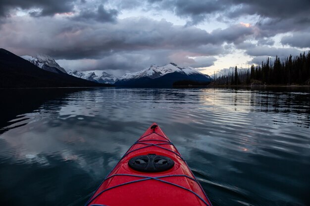 Kayak en un lago glaciar pacífico y tranquilo durante una vibrante puesta de sol nublada