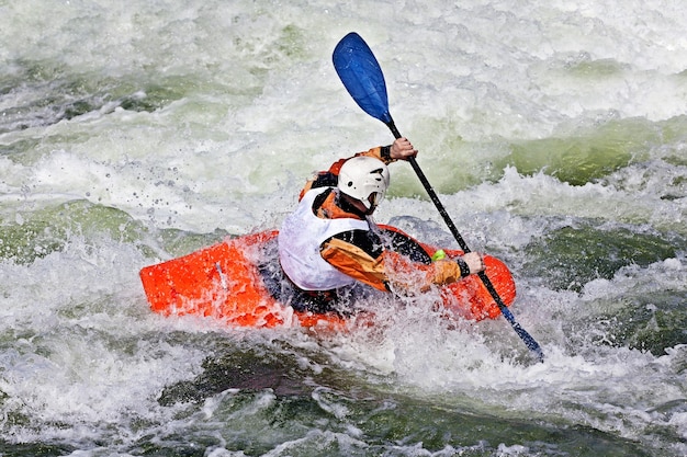 Un kayakista masculino activo rodando y surfeando en aguas turbulentas